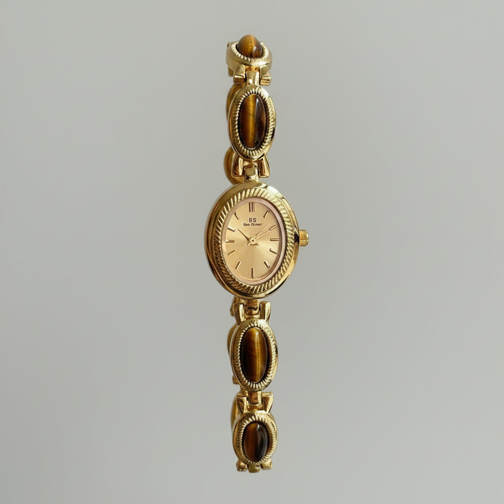 Gold wristwatch with gemstone accents held by a hand against a neutral background