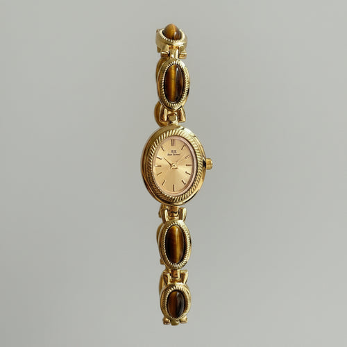 Gold wristwatch with gemstone accents held by a hand against a neutral background